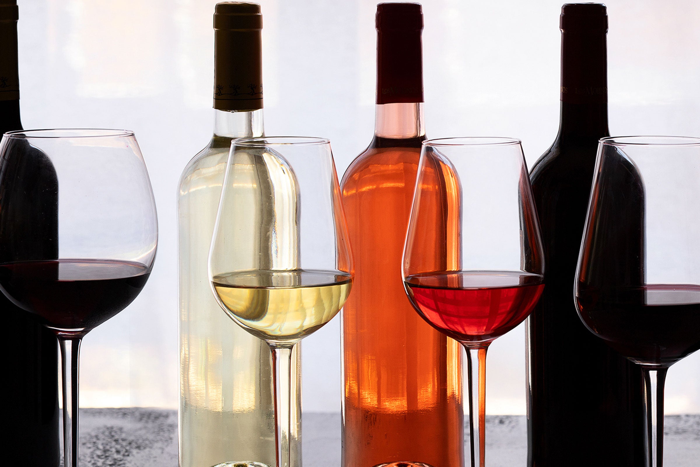 Weinflaschen mit eingeschenkten Weinglaesern davor. Rotwein Weisswein Rosewein